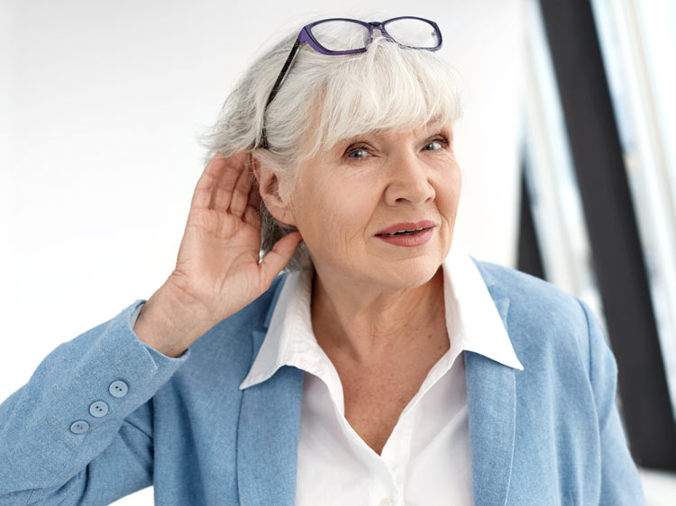 A senior woman with auditory deprivation cups her hand behind her ear to try to hear