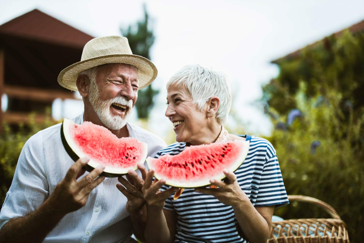 A senior couple wearing Beltone Hearing Aids eat watermelon outside