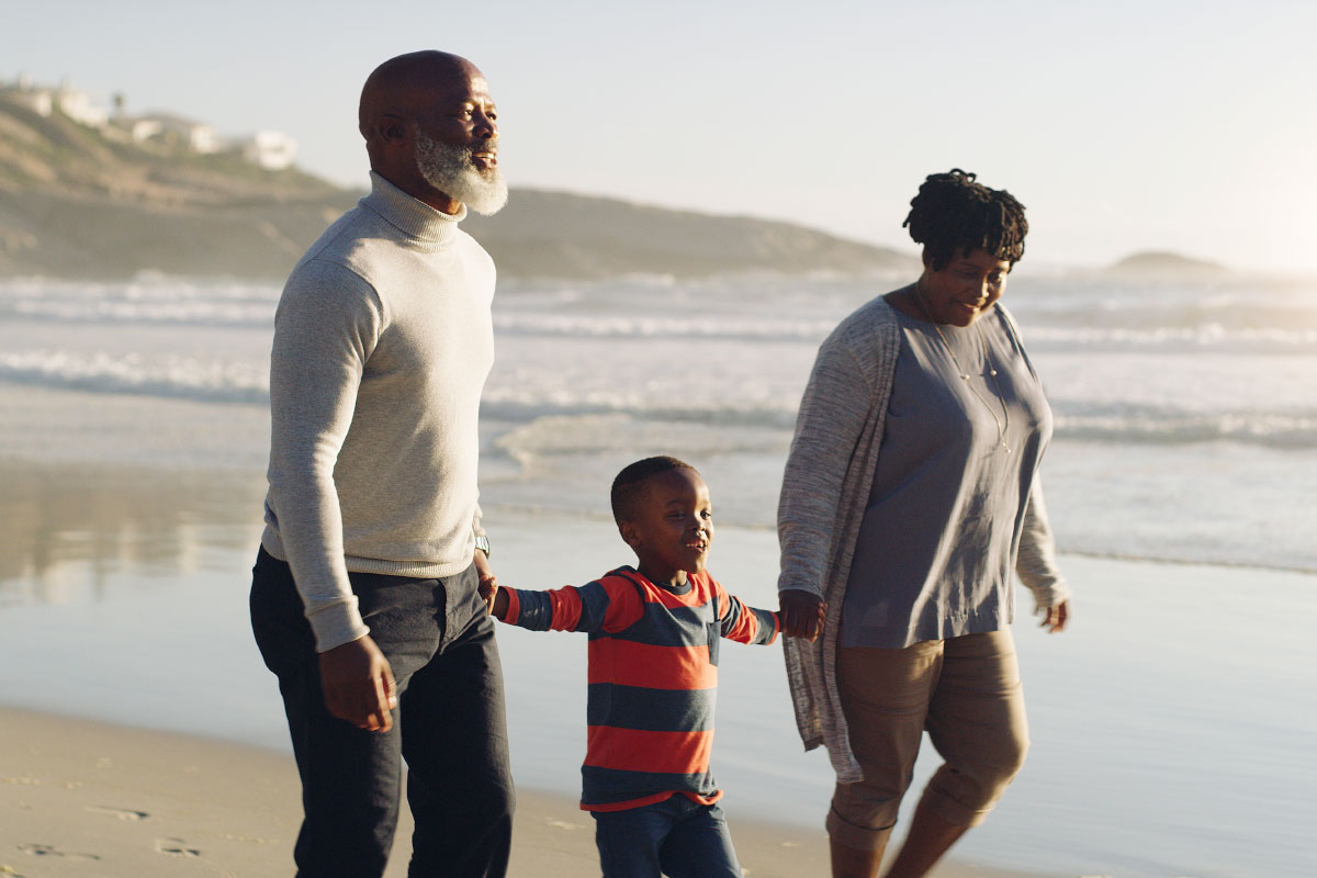 A senior couple that have Beltone Hearing Aids and BelCare walk on a beach with their grandson