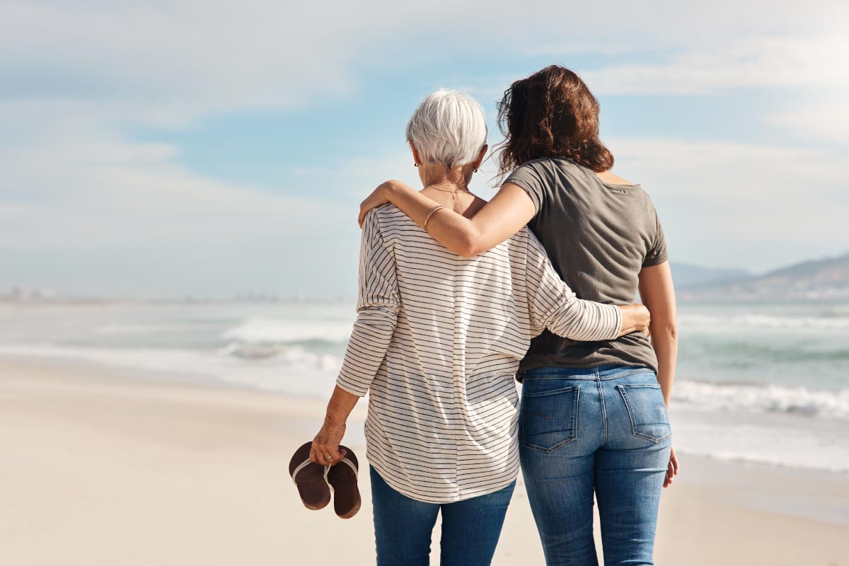 A senior woman with Beltone hearing aids walks with her daughter along the beach