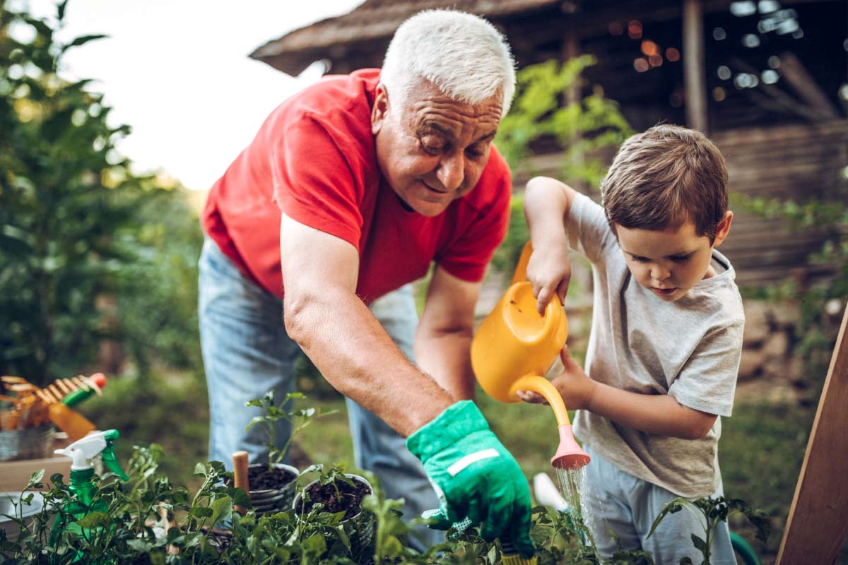 A senior man wearing Beltone hearing aids helps his grandson water his garden