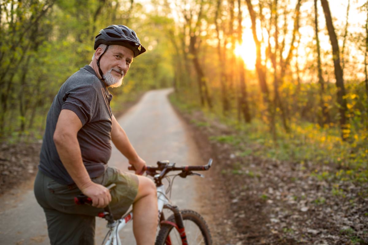 A senior man wearing Beltone Hearing Aids gets on his bike on a long trail