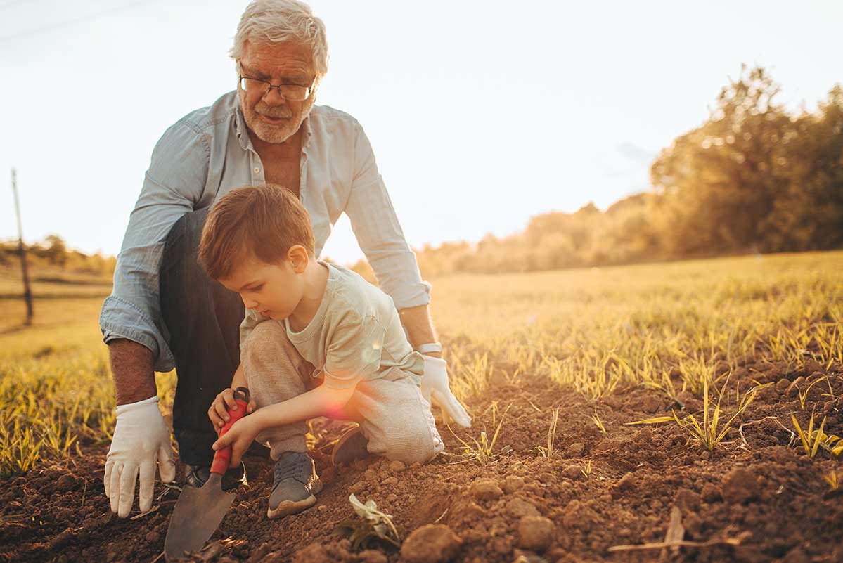 A grandfather wearing Beltone Imagine hearing aids works with his grandson in a garden