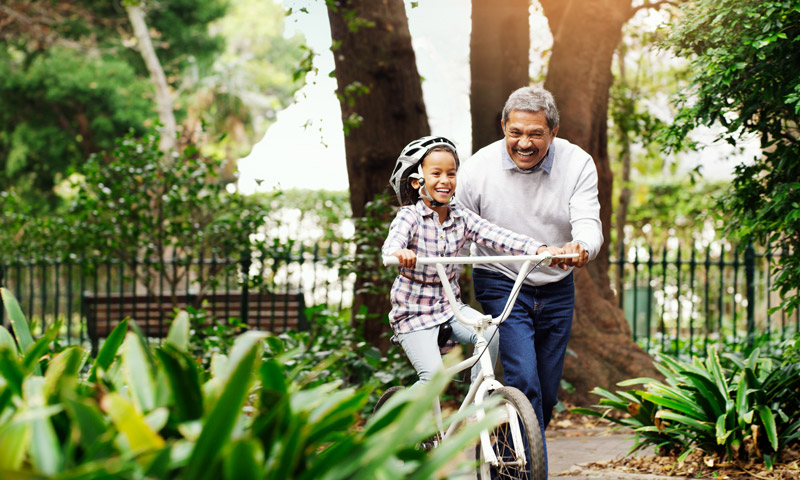 A grandfather guiding his grandchild on a bike in a park