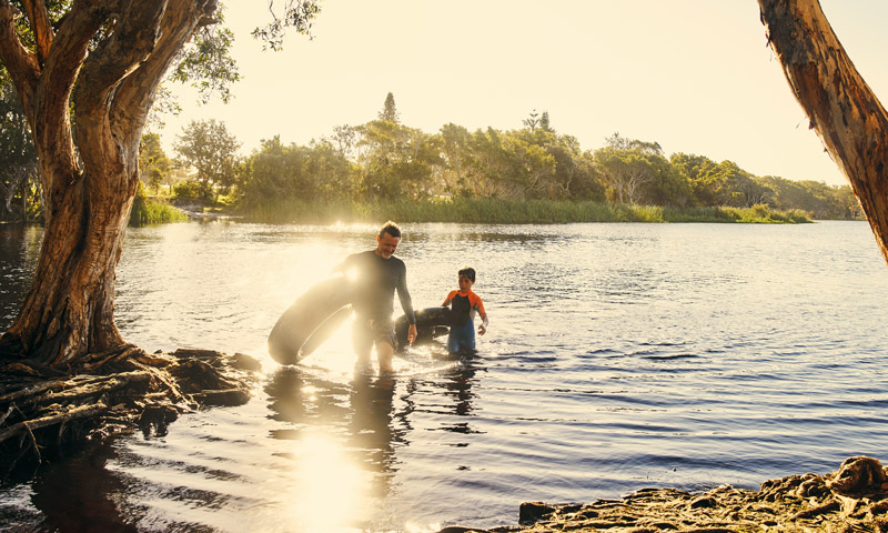Parent and child wading in a river holding inner tubes