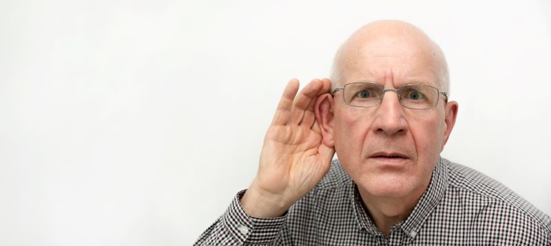 senior man holds one hand to his ear to signal that he can't hear