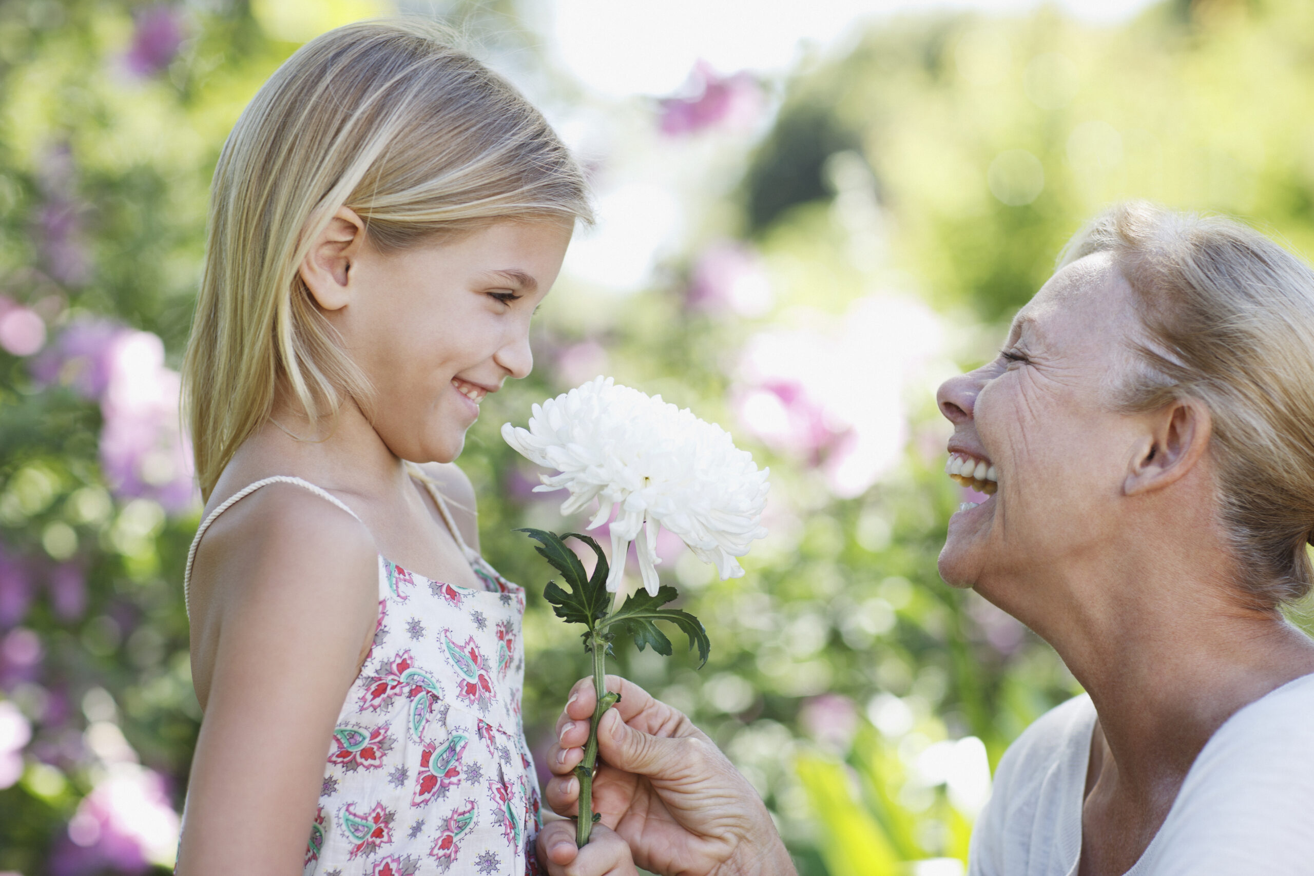 Grandmother giving flower to granddaughter in garden