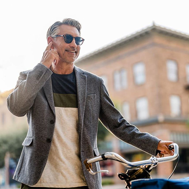 a man wearing sunglasses touches his finger to his ear to take a phone call on his Beltone hearing aids