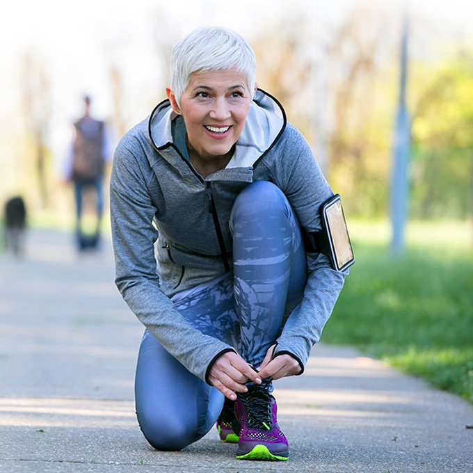A senior woman wearing Beltone Hearing Aids on a run and tying her shoes