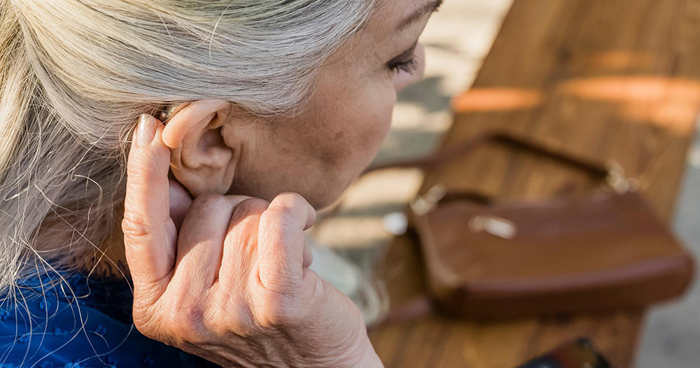 a person pressing a button on their Beltone hearing aid receiver behind their ear