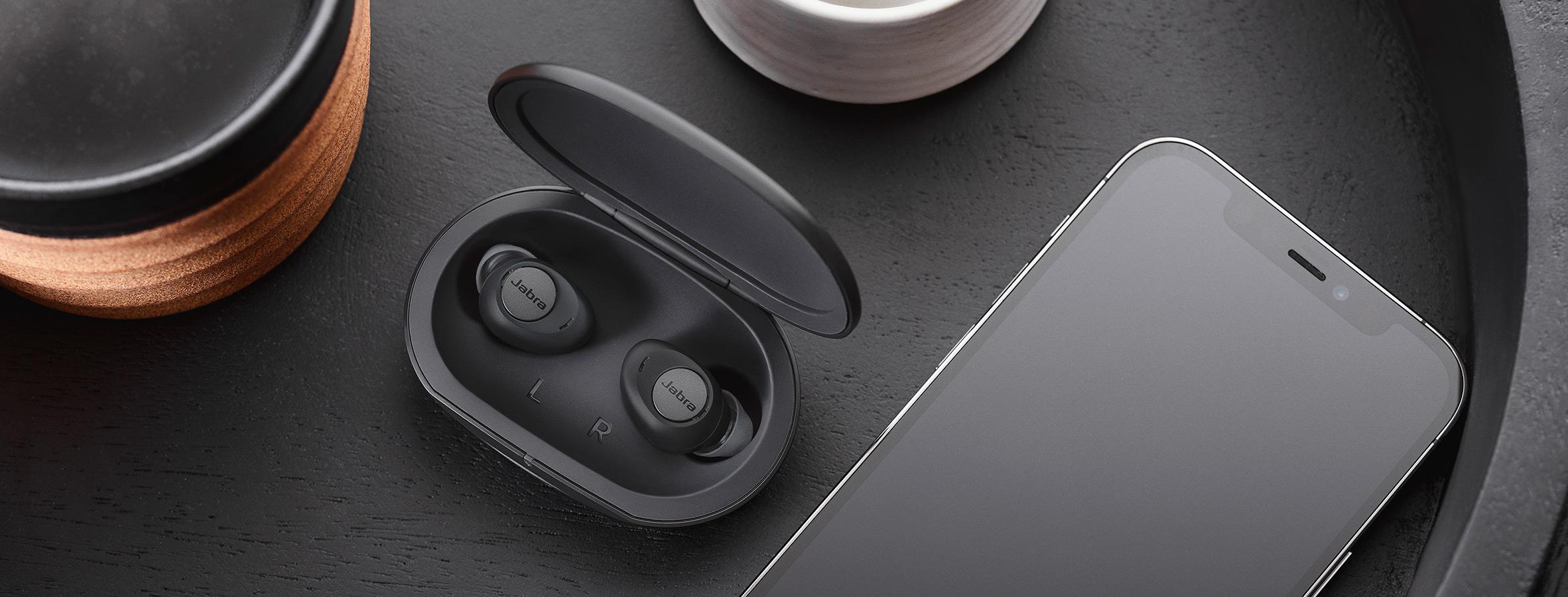 Jabra Enhance™ Plus over-the-counter earbud hearing aids sitting in their charging case on a coffee table