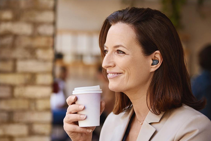 a woman enjoying coffee while wearing Jabra Enhance™ Plus over-the-counter earbud hearing aids