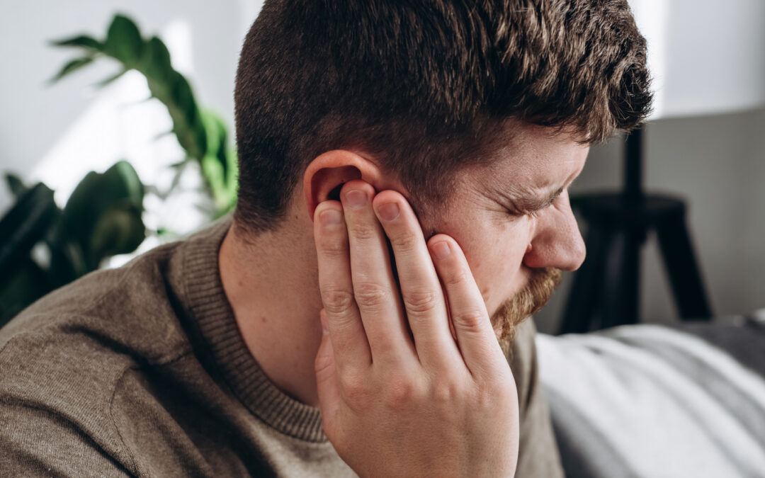 Close-up of unhealthy young caucasian man 30s touching ear, suffering from sudden throbbing ear ache.