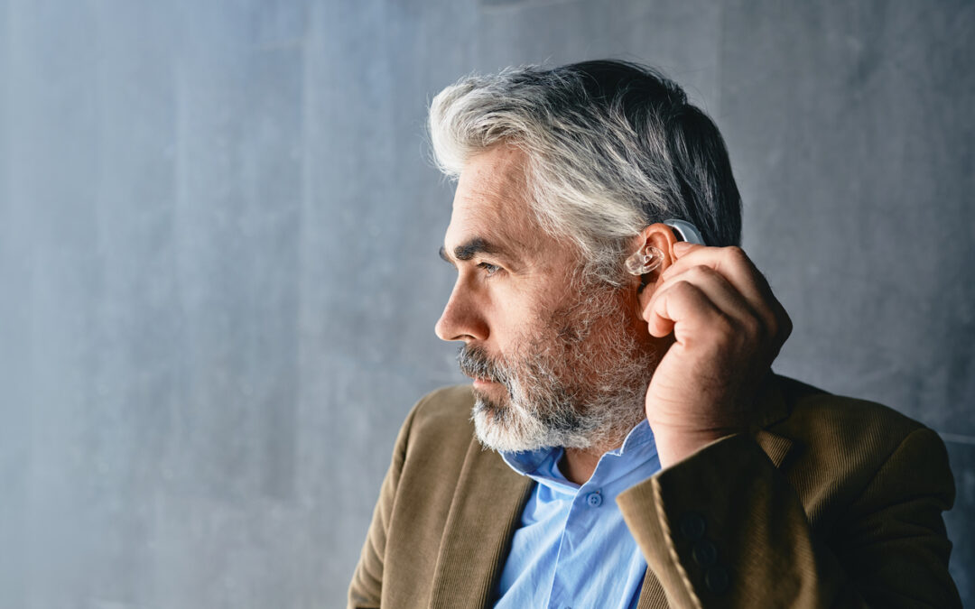 Grey-haired mature man with hearing impairment using hearing aid